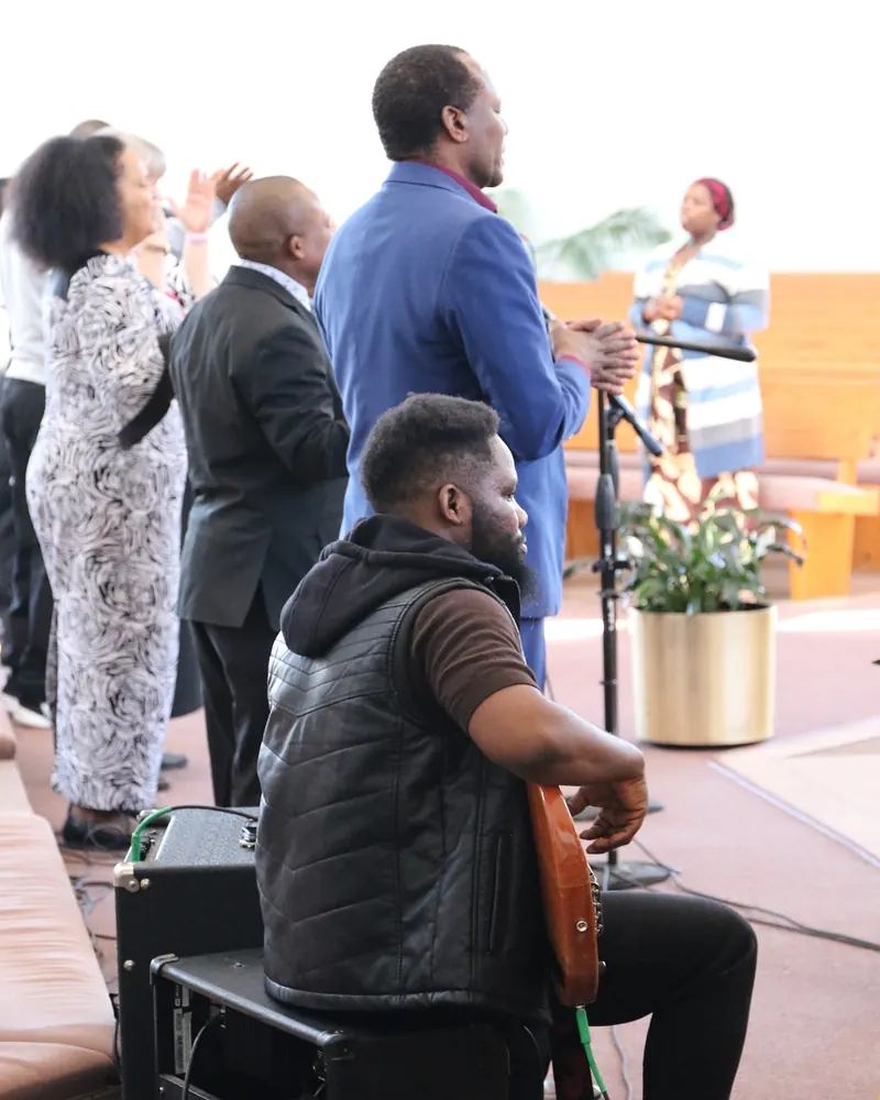 Members singing and praising together at an outreach gathering, with a guitarist seated in front